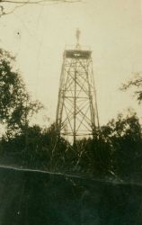 Lightkeeper standing at the top of a tower constructed of timber cut on the spot in central Alaska. Image
