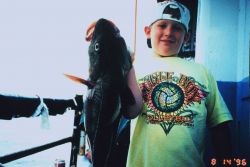 A young fisherman proudly displays a fish almost as large as himself Image