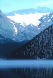 Mist below and glacier above while a high rocky peak dominates all. Image