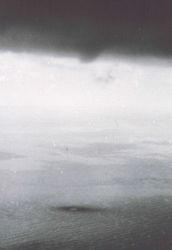 Dark spot on water surface indicates end-point of invisible funnel emanating from short protrusion on right-center of cloud base. Image