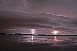 Lightning in the distance seen over bay waters. Image