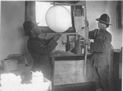 Signal Corps meteorological students Bly and Greening using an improvised caliper to assure weather balloon is properly inflated prior to launching. Image