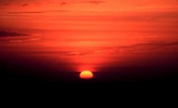 Sun approaching the horizon as the bottom limb is becoming obscured by far distant clouds. Photo