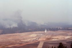 View of Old Faithful Geyser, smoldering fire & smoke from Old Faithful Inn crow's nest Image